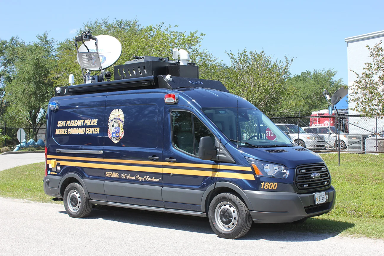 Passenger's side of a CRU-22 Mobile Command vehicle parked near the Frontline Communications building on a sunny day.
