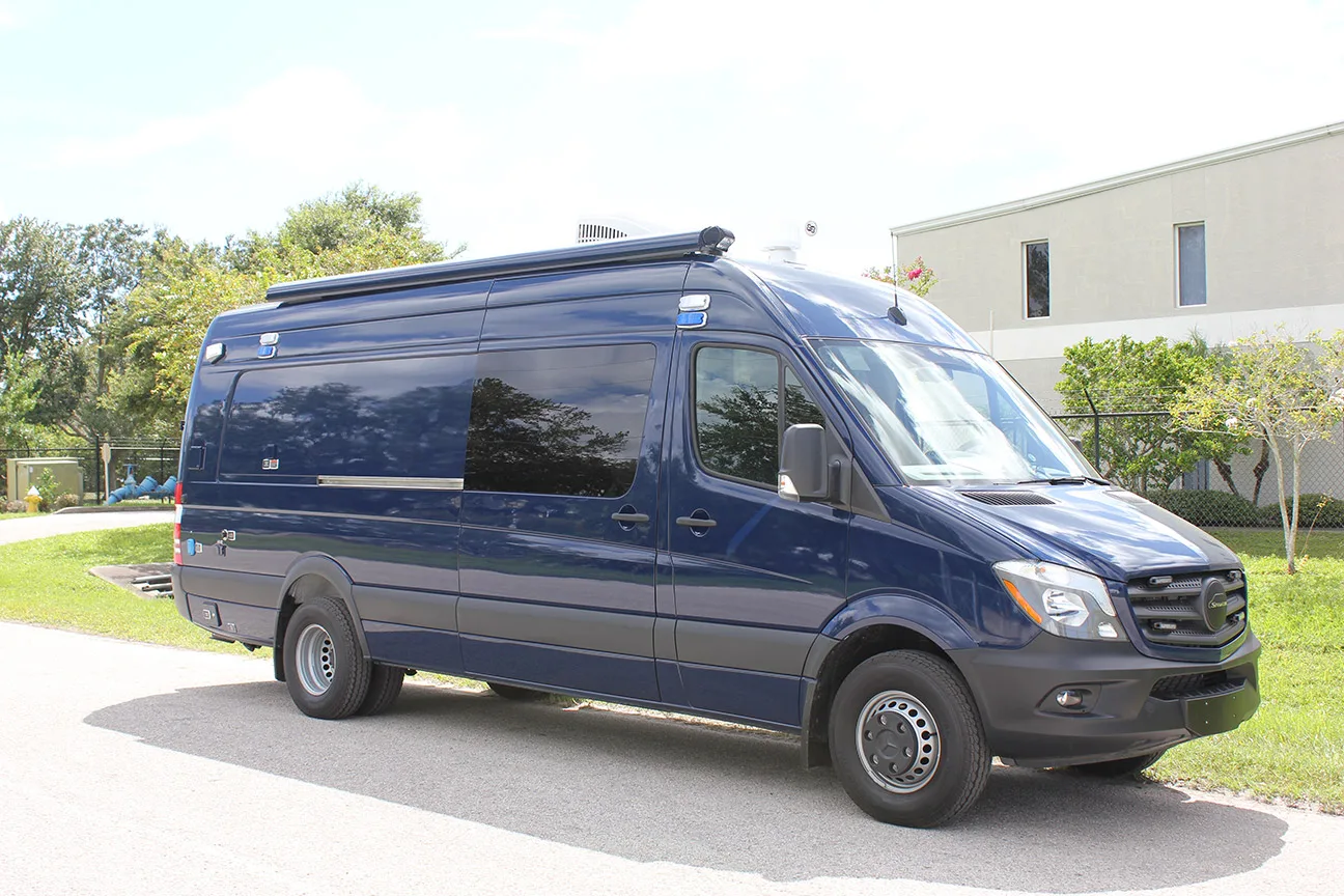 Blue Mobile Precinct vehicle parked outside in front of the Frontline Communications building on a sunny day.