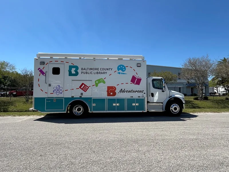 Baltimore Public Library C-35 Mobile Library Specialty Vehicle parked outside of the Frontline Communications vehicle on a sunny day.