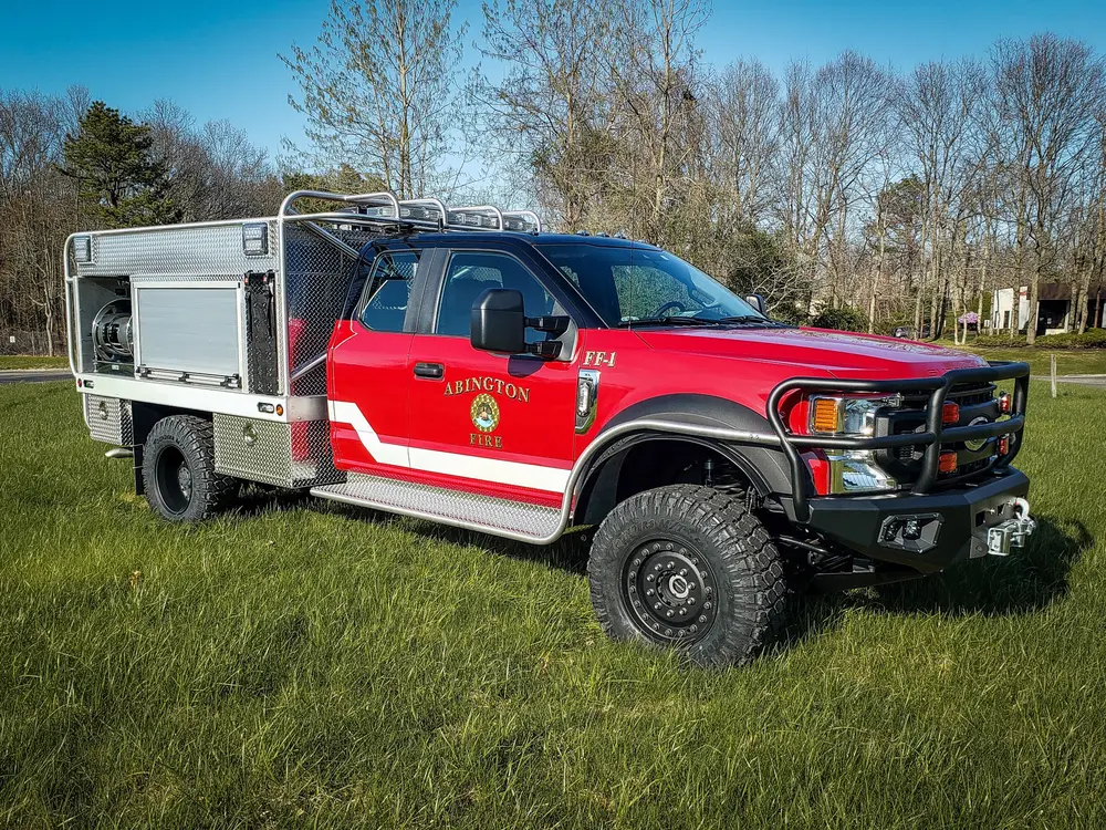 Exterior view of small fire truck showing cab, body compartments, and wheel/tire area.