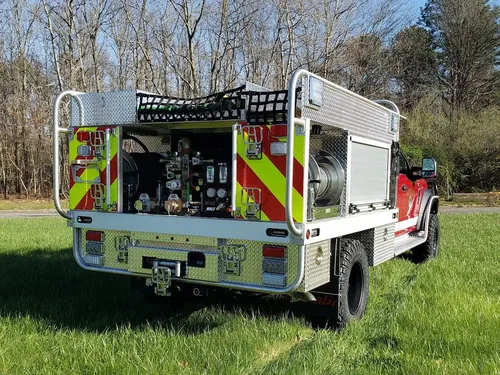 Exterior view of small fire truck showing cab, body compartments, and wheel/tire area.
