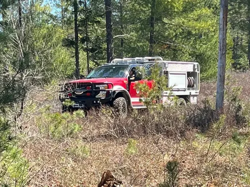 Exterior view of small fire truck showing cab, body compartments, and wheel/tire area.