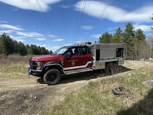 Exterior view of small fire truck showing cab, body compartments, and wheel/tire area.
