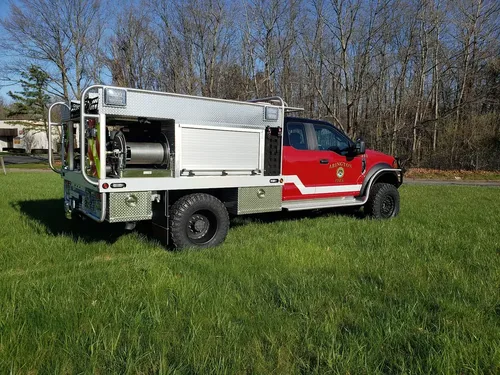 Exterior view of small fire truck showing cab, body compartments, and wheel/tire area.