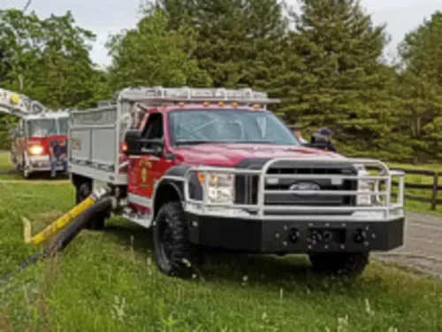 Exterior view of small fire truck showing cab, body compartments, and wheel/tire area.