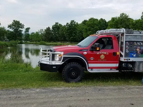 Exterior view of small fire truck showing cab, body compartments, and wheel/tire area.