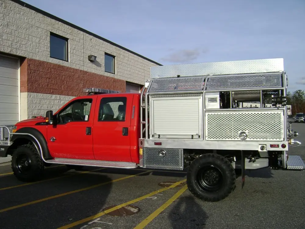 Exterior view of small fire truck showing cab, body compartments, and wheel/tire area.