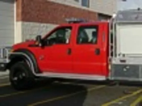 Exterior view of small fire truck showing cab, body compartments, and wheel/tire area.