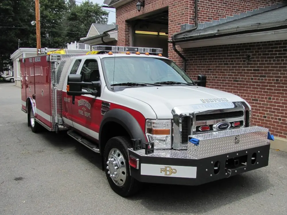 Exterior view of small fire truck showing cab, body compartments, and wheel/tire area.