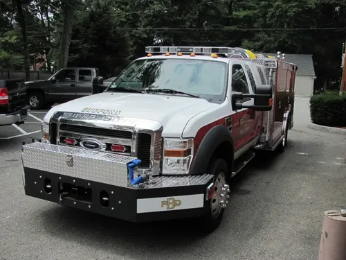 Exterior view of small fire truck showing cab, body compartments, and wheel/tire area.