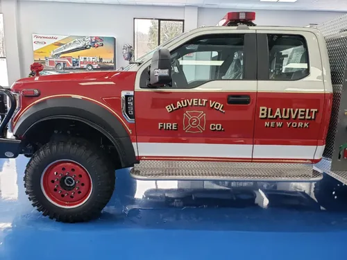 Exterior view of small fire truck showing cab, body compartments, and wheel/tire area.
