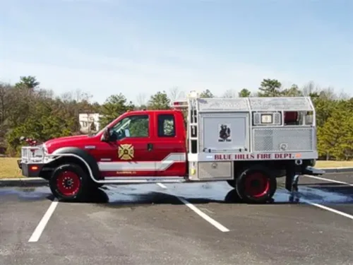 Exterior view of small fire truck showing cab, body compartments, and wheel/tire area.