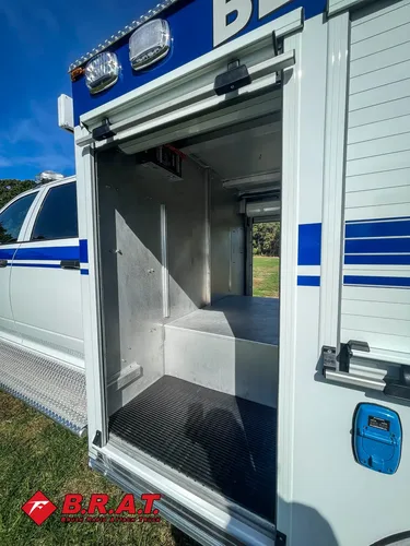 Exterior view of small fire truck showing cab, body compartments, and wheel/tire area.