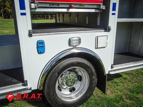 Exterior view of small fire truck showing cab, body compartments, and wheel/tire area.