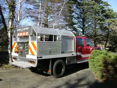 Exterior view of small fire truck showing cab, body compartments, and wheel/tire area.