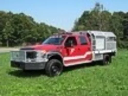 Exterior view of small fire truck showing cab, body compartments, and wheel/tire area.