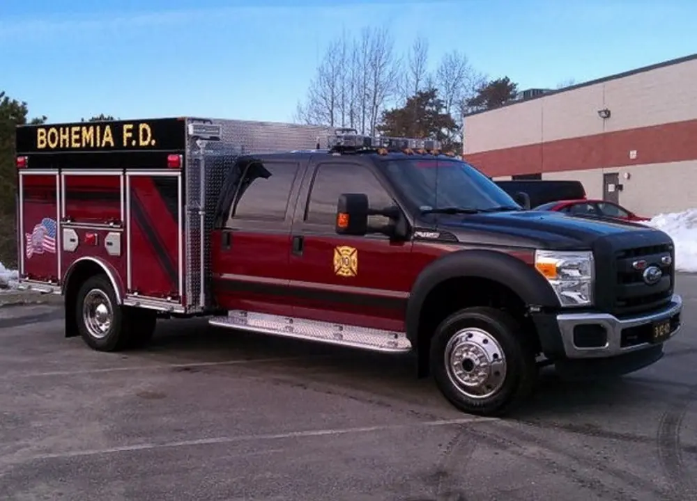 Exterior view of small fire truck showing cab, body compartments, and wheel/tire area.
