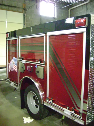 Exterior view of small fire truck showing cab, body compartments, and wheel/tire area.