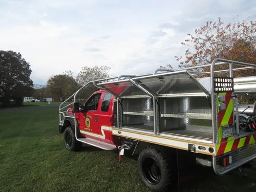 Exterior view of small fire truck showing cab, body compartments, and wheel/tire area.