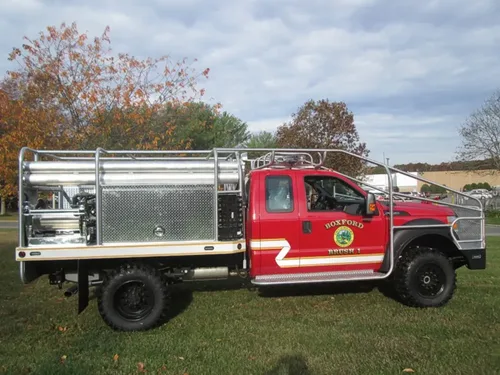 Exterior view of small fire truck showing cab, body compartments, and wheel/tire area.