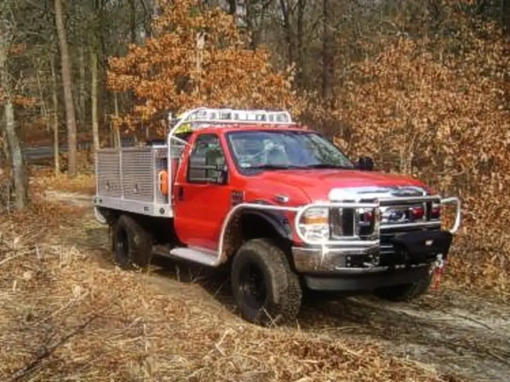 Exterior view of small fire truck showing cab, body compartments, and wheel/tire area.