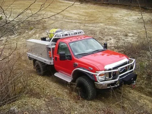 Exterior view of small fire truck showing cab, body compartments, and wheel/tire area.