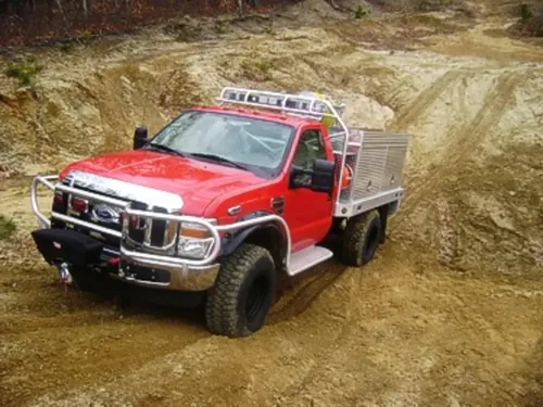 Exterior view of small fire truck showing cab, body compartments, and wheel/tire area.