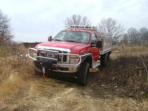 Exterior view of small fire truck showing cab, body compartments, and wheel/tire area.