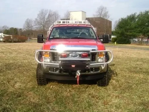 Exterior view of small fire truck showing cab, body compartments, and wheel/tire area.