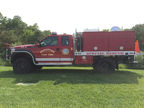 Exterior view of small fire truck showing cab, body compartments, and wheel/tire area.