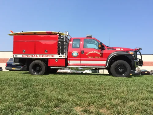 Exterior view of small fire truck showing cab, body compartments, and wheel/tire area.
