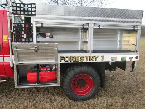 Exterior view of small fire truck showing cab, body compartments, and wheel/tire area.