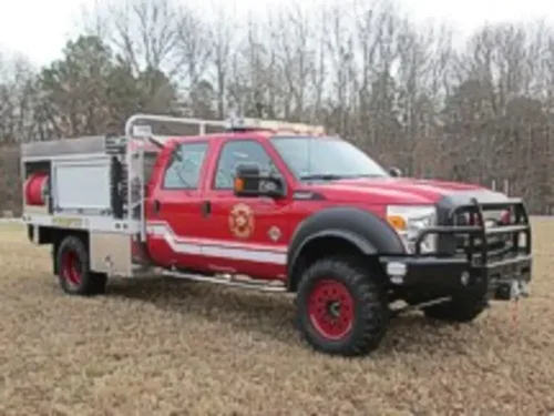 Exterior view of small fire truck showing cab, body compartments, and wheel/tire area.
