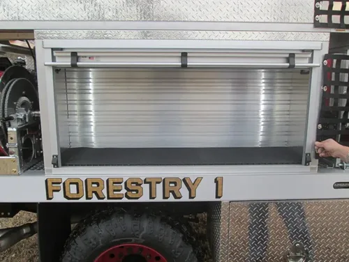Exterior view of small fire truck showing cab, body compartments, and wheel/tire area.