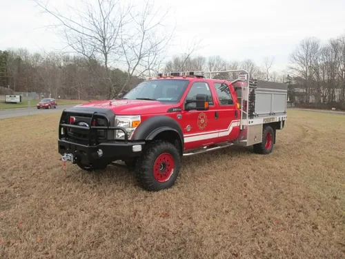 Exterior view of small fire truck showing cab, body compartments, and wheel/tire area.