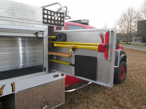 Exterior view of small fire truck showing cab, body compartments, and wheel/tire area.