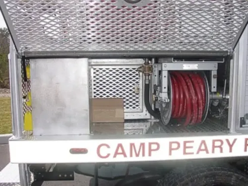 Exterior view of small fire truck showing cab, body compartments, and wheel/tire area.