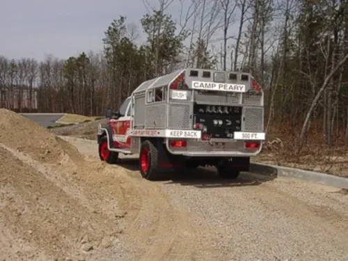 Exterior view of small fire truck showing cab, body compartments, and wheel/tire area.