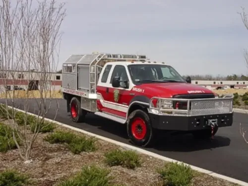 Exterior view of small fire truck showing cab, body compartments, and wheel/tire area.