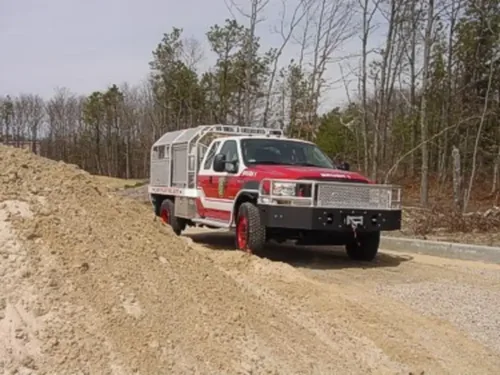 Exterior view of small fire truck showing cab, body compartments, and wheel/tire area.