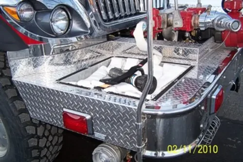 Exterior view of small fire truck showing cab, body compartments, and wheel/tire area.