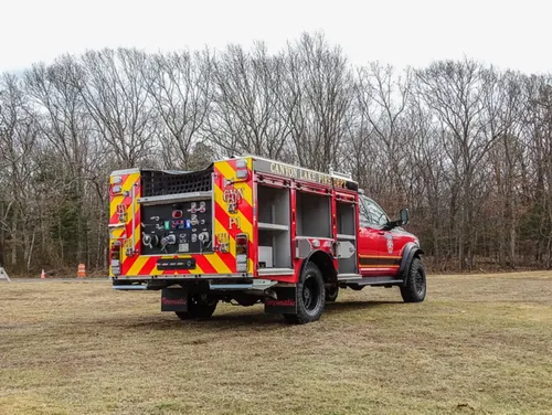 Exterior view of small fire truck showing cab, body compartments, and wheel/tire area.