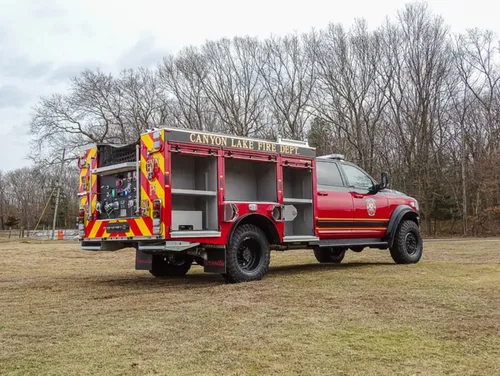 Exterior view of small fire truck showing cab, body compartments, and wheel/tire area.