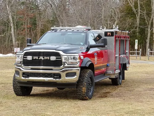Exterior view of small fire truck showing cab, body compartments, and wheel/tire area.