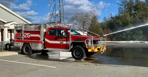 Exterior view of small fire truck showing cab, body compartments, and wheel/tire area.