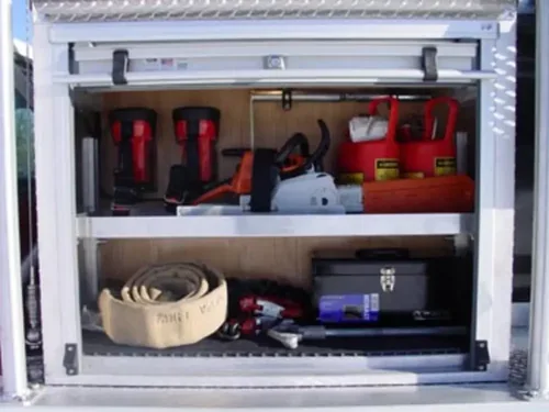 Exterior view of small fire truck showing cab, body compartments, and wheel/tire area.