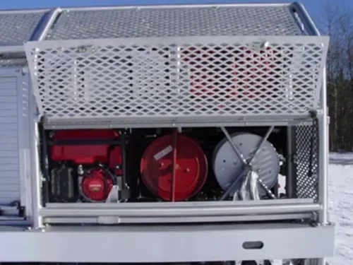 Exterior view of small fire truck showing cab, body compartments, and wheel/tire area.