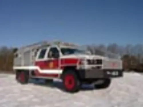 Exterior view of small fire truck showing cab, body compartments, and wheel/tire area.