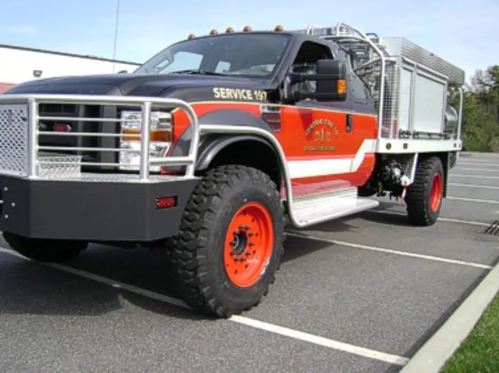 Exterior view of small fire truck showing cab, body compartments, and wheel/tire area.