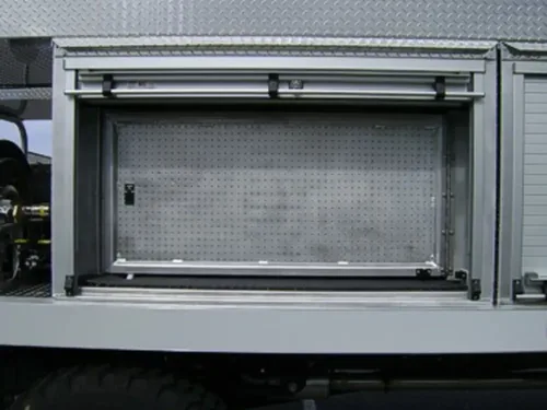 Exterior view of small fire truck showing cab, body compartments, and wheel/tire area.